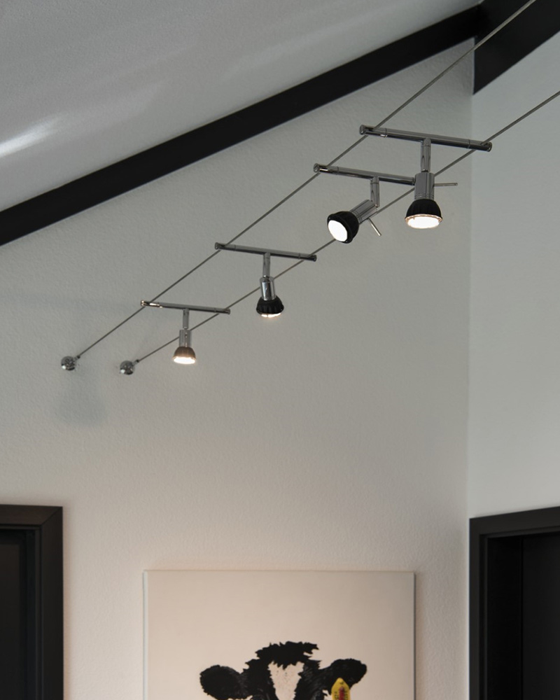 Seilsystem mit modernen Strahlern in einem Zimmer mit schräger Decke Seilsystem mit modernen Strahlern in einem Zimmer mit schräger Decke