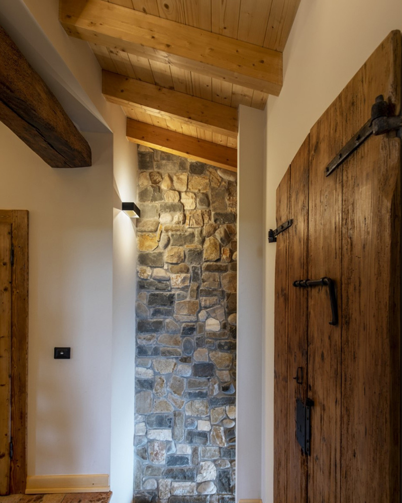 Schlicht beleuchtetes altes Dachzimmer mit Steinwand, Holztüren und Holzbalken Schlicht beleuchtetes altes Dachzimmer mit Steinwand, Holztüren und Holzbalken