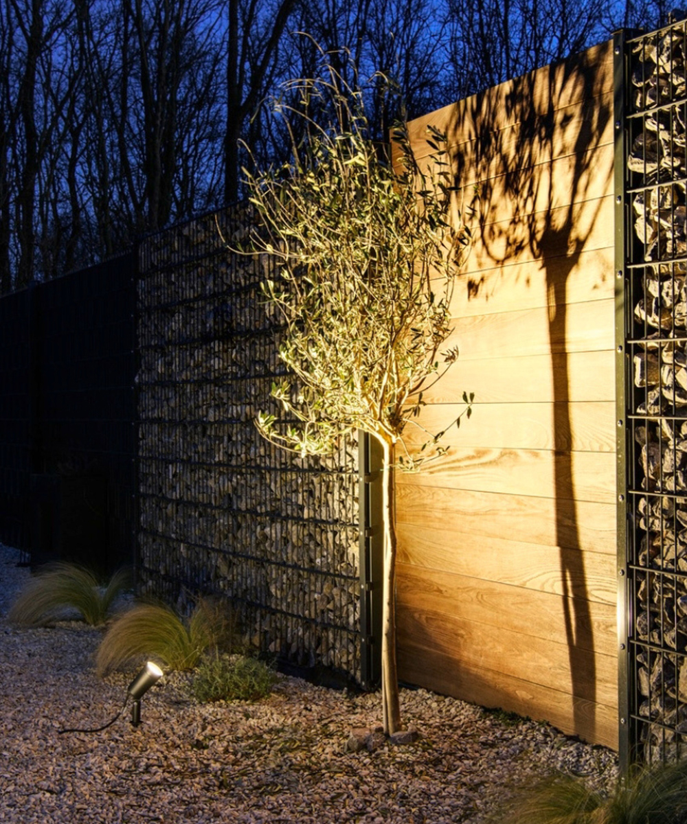 Direkte Beleuchtung eines Gartenmauersegments aus Holz durch einen im Boden verankerten Außenstrahler