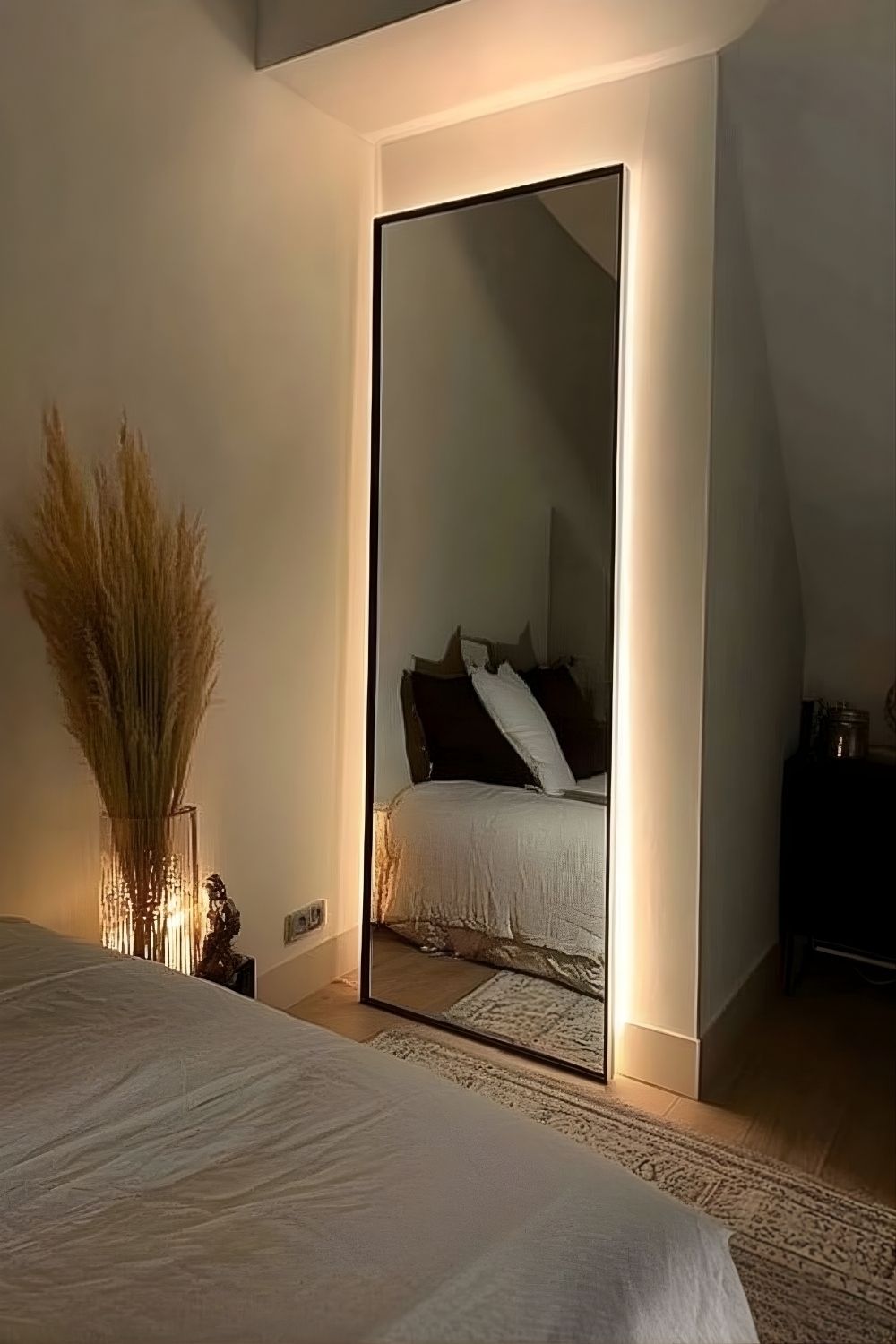 Schlafzimmer mit indirekter Wandbeleuchtung hinter hohem Spiegel und großer Pflanzenvase